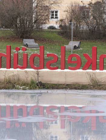 Dinkelsbühl, ein Genussort am 2. Adventswochenende? Das Foto zeigt in großen roten Buchstaben das Wort Dinkelsbühl, das am Stadtpark als überdimensionale Grafikskulptur steht. Davor ist ein zugefrohrener See, dahinter sieht man drei kleinere Häuser mit dezentem Fachwerk.